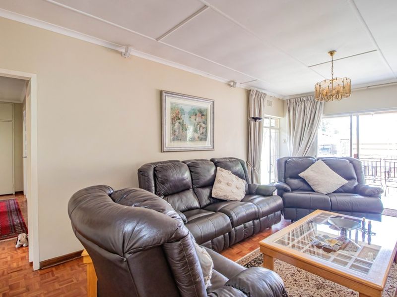 A spacious living room featuring classic parquet flooring, large sliding glass doors providing natural light, and access to an outdoor patio area.