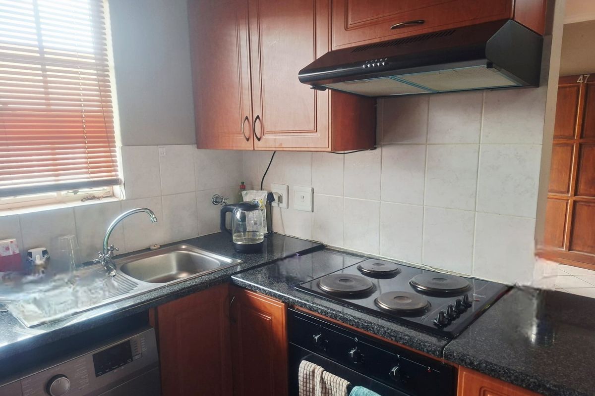 Compact kitchen featuring wooden cabinetry, dark laminate countertops, a built-in oven with electric hob, extractor fan, and a stainless steel sink.