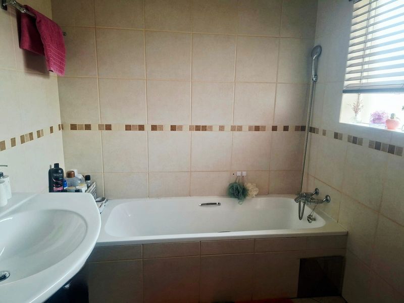 A functional bathroom featuring a bathtub with a handheld shower mixer, tiled wall finishes, and a window with fitted venetian blinds.