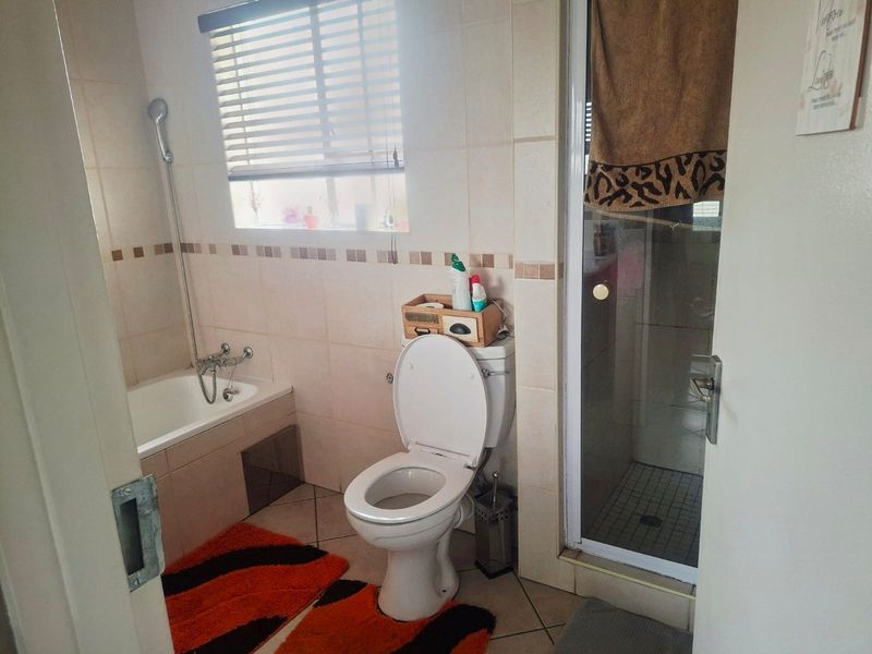 A functional bathroom featuring a built-in bathtub, separate shower enclosure, and toilet, finished with neutral wall and floor tiles.