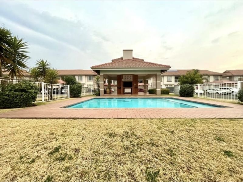 Communal swimming pool area featuring a covered entertainment pavilion with a built-in braai, set within a landscaped residential complex.