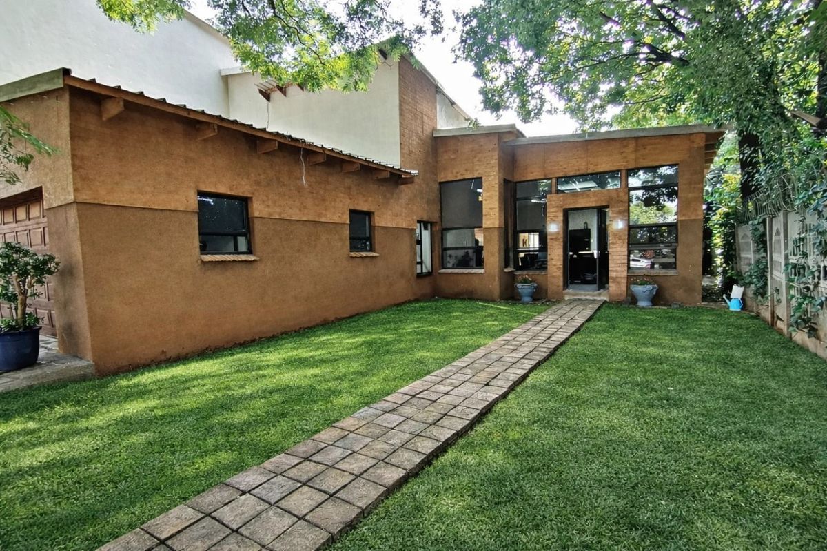 Rear view of the property featuring a paved walkway leading to the entrance, a well-maintained lawn, and textured exterior walls.