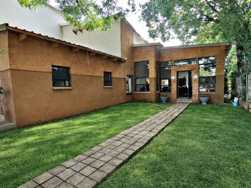 Rear view of the property featuring a paved walkway leading to the entrance, a well-maintained lawn, and textured exterior walls.