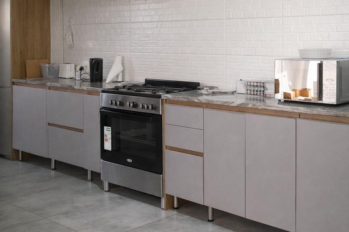 Modern kitchen featuring light grey cabinetry, stone countertops, a gas stove with oven, and a white tiled backsplash.