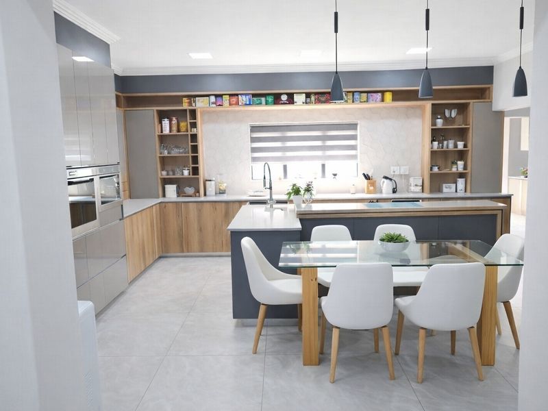 Modern open-plan kitchen featuring high-gloss cabinetry, stone countertops, a central island, and integrated appliances, seamlessly flowing into the dining area.