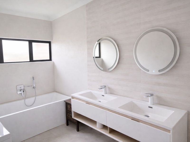 Modern bathroom featuring a double vanity with integrated mirrors, a built-in bathtub with wall-mounted fixtures, and neutral tiled finishes.