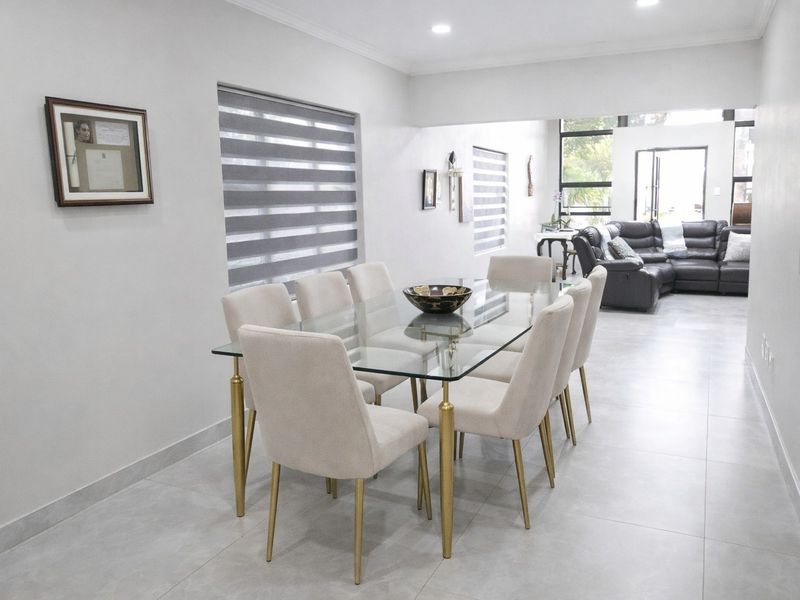 Spacious open-plan dining area featuring neutral tiled flooring, recessed downlighting, and modern roller blinds, flowing seamlessly into the adjacent living space.