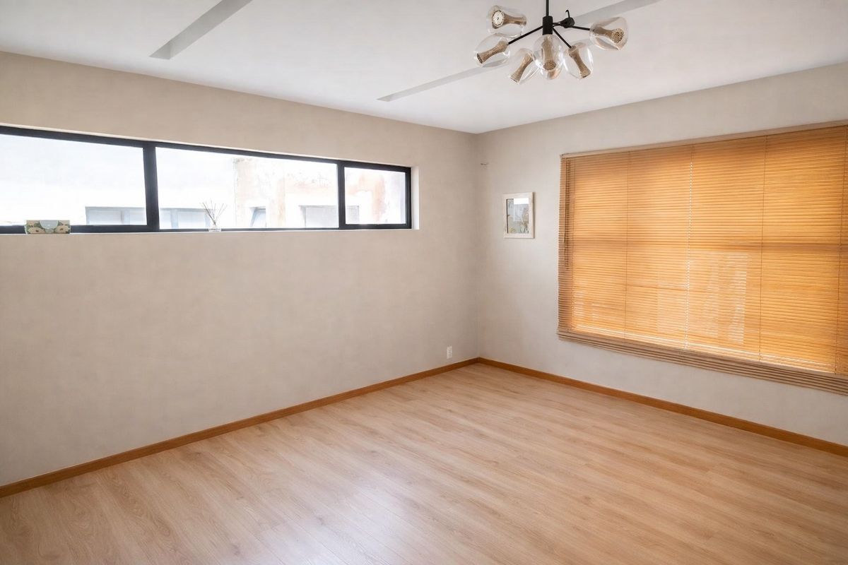 A bright and spacious bedroom featuring light laminate flooring, modern lighting, and large windows with timber venetian blinds.
