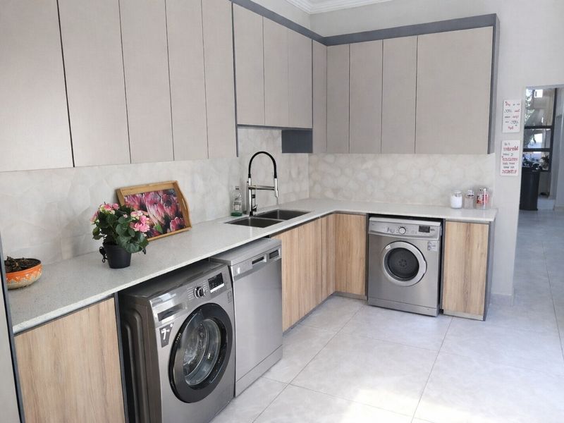 Modern scullery featuring sleek built-in cabinetry, stone countertops, a double sink with a contemporary mixer tap, and integrated space for laundry appliances.
