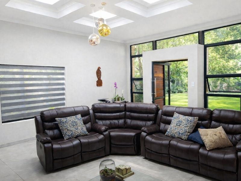 Spacious living room featuring a modern coffered ceiling, large black-framed windows providing garden views, and sleek tiled flooring.