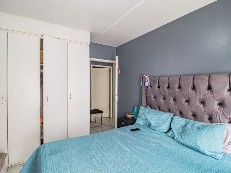 A bedroom featuring built-in cupboards and a neutral grey accent wall, providing a functional space with standard finishes.