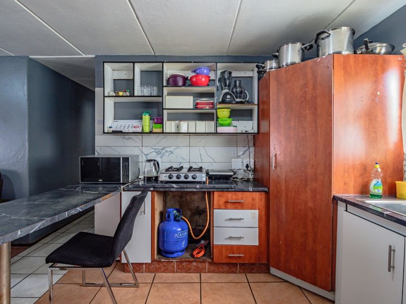 A compact kitchen featuring built-in wooden cabinetry, a gas hob, tiled backsplash, and a stainless steel sink, requiring some maintenance and cosmetic updates.