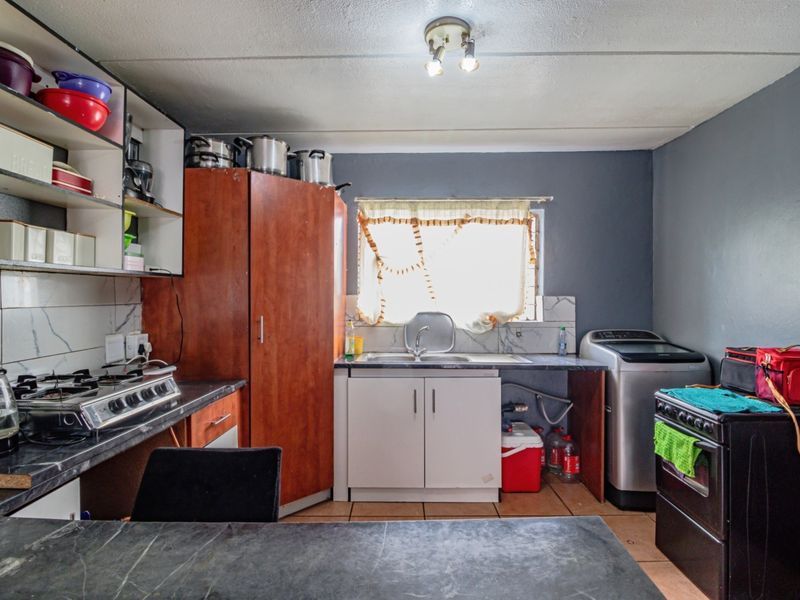 Functional kitchen featuring built-in cabinetry, laminate countertops, a stainless steel sink, and a tiled backsplash, offering a practical layout for daily meal preparation.