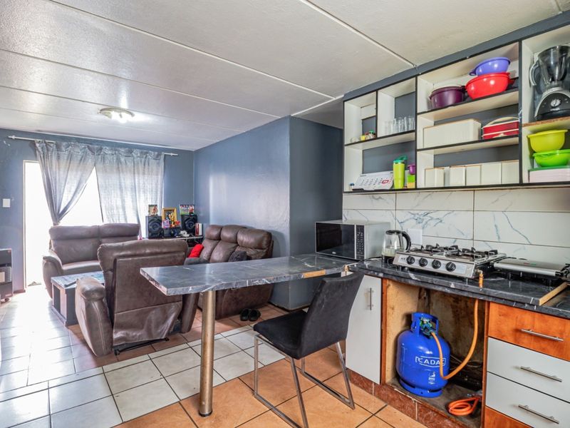 Open-plan living and kitchen area featuring tiled flooring, a breakfast bar, and a compact kitchen setup with open shelving and a gas hob.