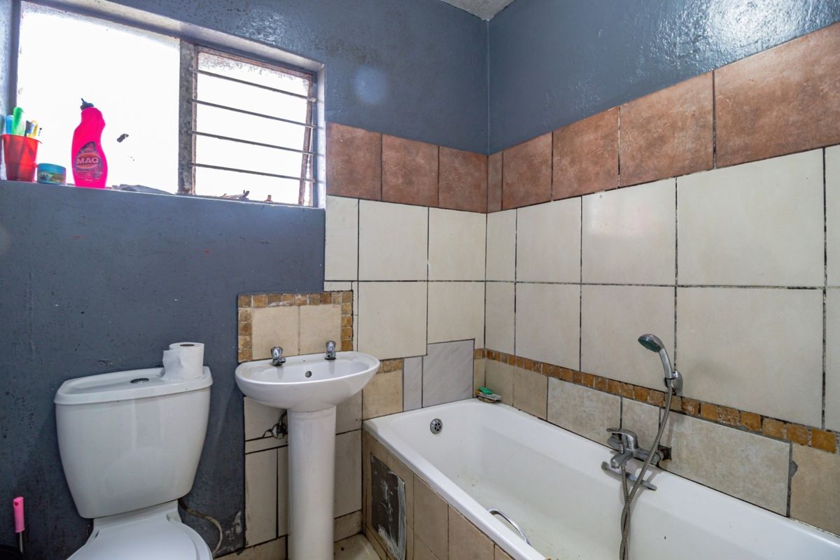 A dated bathroom featuring a pedestal basin, toilet, and bathtub with handheld shower mixer, requiring cosmetic updates and tile repairs.