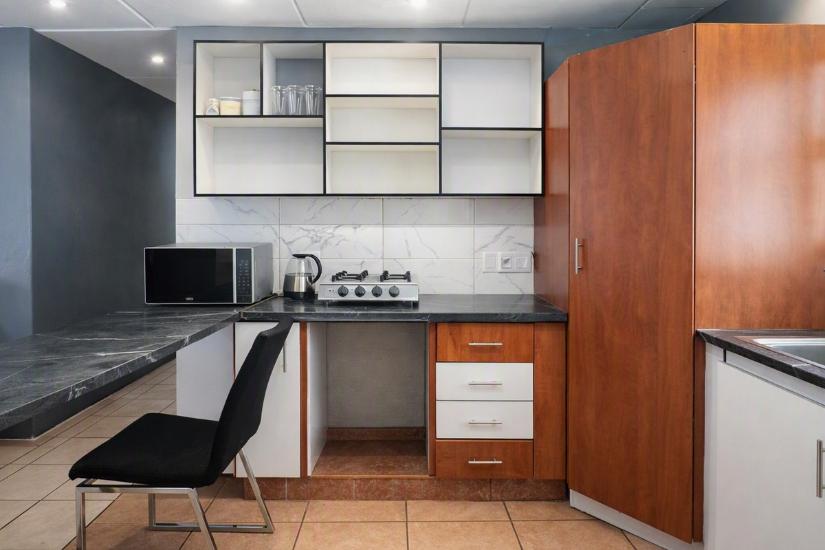 Compact kitchen featuring marble-effect countertops, gas hob, built-in cabinetry, and a breakfast bar extension, offering functional preparation space.