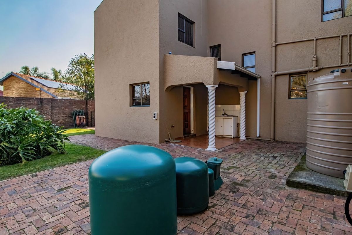 Rear exterior view featuring a paved courtyard, covered patio area with a sink, and a large water storage tank.