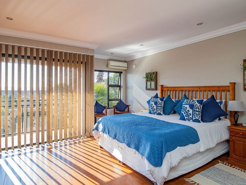 Spacious bedroom featuring laminate flooring, recessed lighting, a split-system air conditioner, and large sliding glass doors leading to a private balcony.
