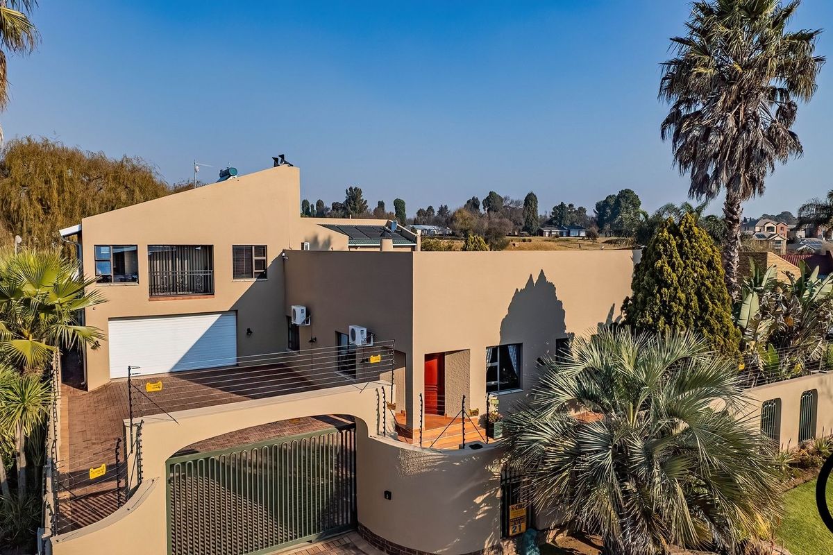 Aerial view of a modern residential property featuring a paved driveway, secure boundary wall with electric fencing, and a double-story house structure.