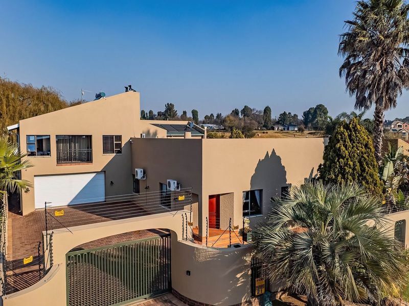 Aerial view of a modern residential property featuring a paved driveway, secure boundary wall with electric fencing, and a double-story house structure.