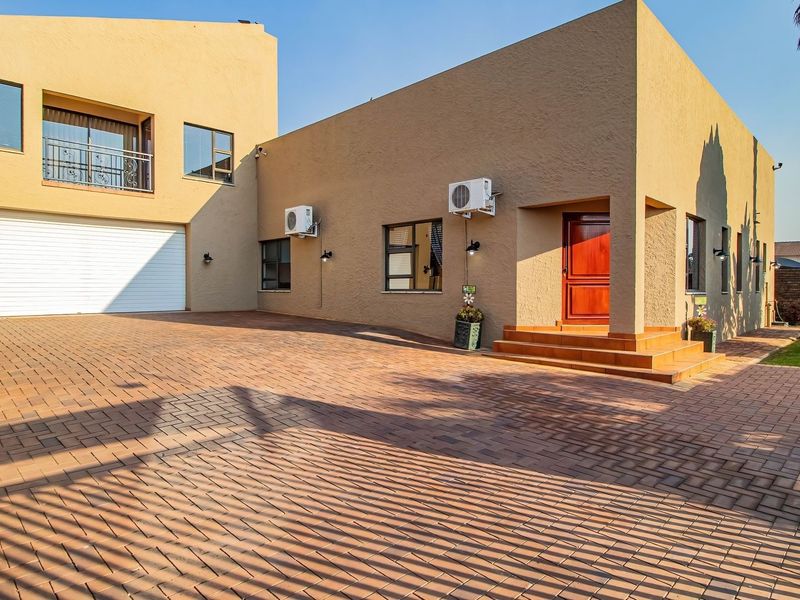 Front elevation of a modern house featuring a spacious paved driveway, double garage, and a welcoming entrance with tiled steps.