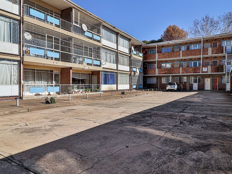 Exterior view of a multi-story apartment complex featuring brick facades, metal balcony railings, and a shared concrete parking area.