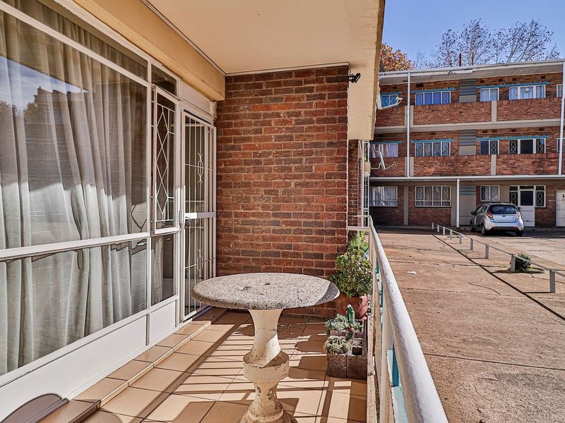 A functional balcony area featuring tiled flooring, a brick feature wall, and secure sliding glass access to the apartment interior.