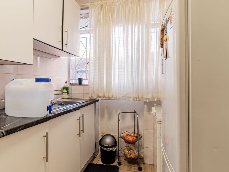 Compact kitchen featuring white cabinetry, dark laminate countertops, tiled backsplash, and a window with security gate, offering a functional layout for renovation.