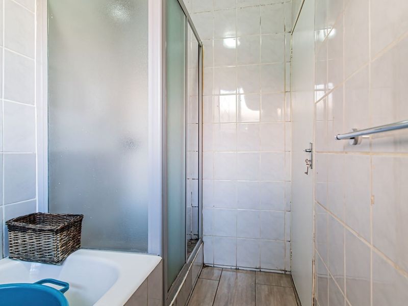A functional bathroom featuring a shower enclosure with tiled walls and flooring, providing a clean, neutral base for potential modernization.