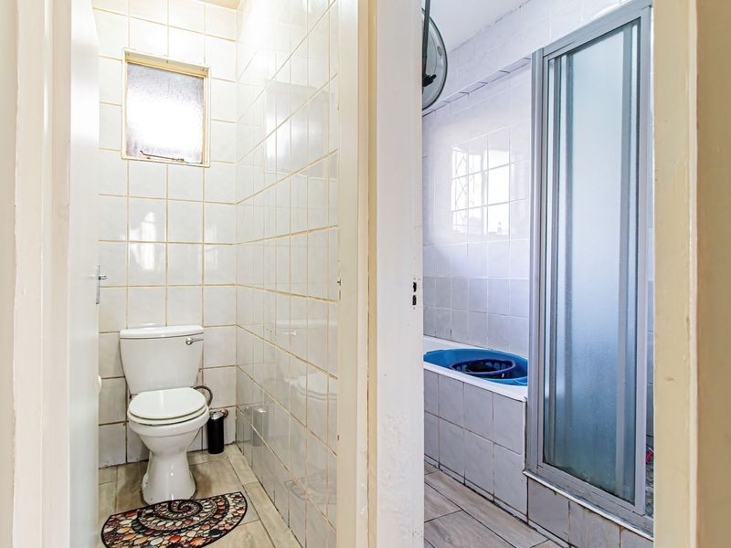 A functional bathroom featuring a separate toilet area, a bathtub, and a shower enclosure with tiled finishes throughout.