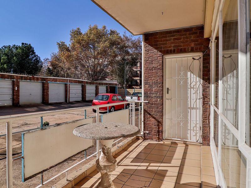 A functional balcony area featuring tiled flooring, a metal security gate, and a metal balustrade, overlooking the apartment complex parking area.
