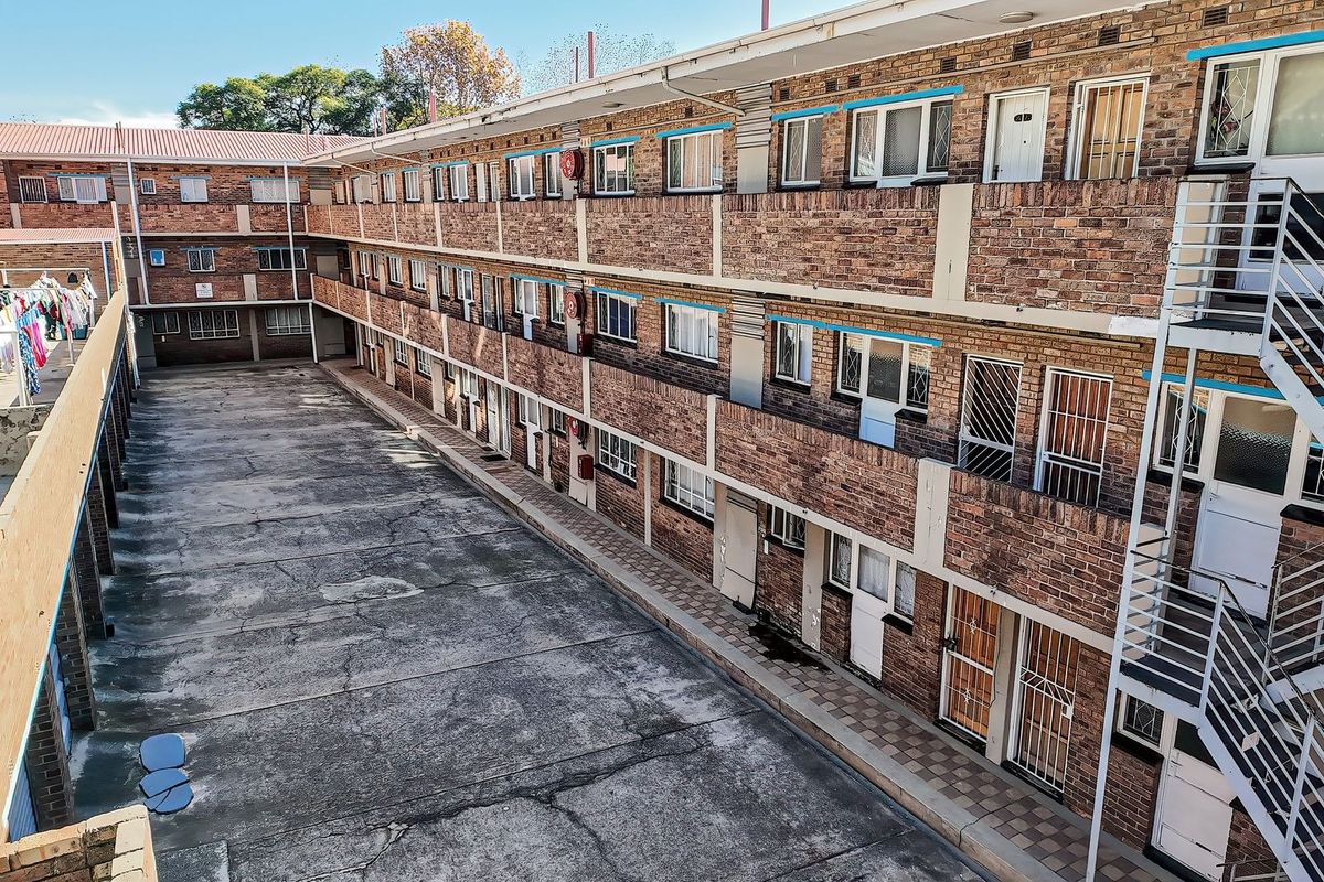 An elevated view of an apartment complex rear courtyard featuring face brick architecture, external staircases, and paved communal areas.