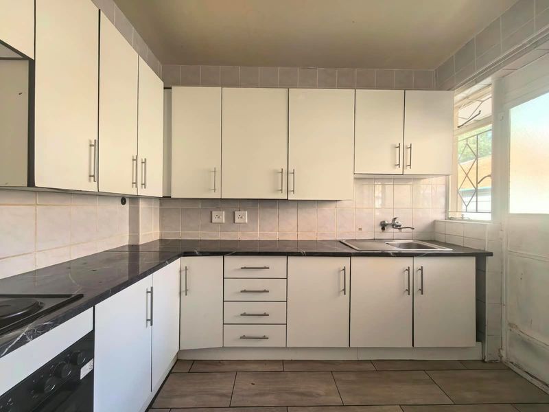 A functional kitchen featuring white cabinetry, dark laminate countertops, a stainless steel sink, and tiled flooring with a built-in oven.