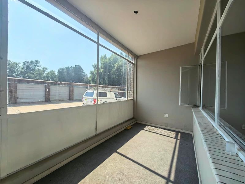 An enclosed balcony area featuring large windows, carpeted flooring, and neutral wall finishes, offering a versatile space for potential conversion or relaxation.