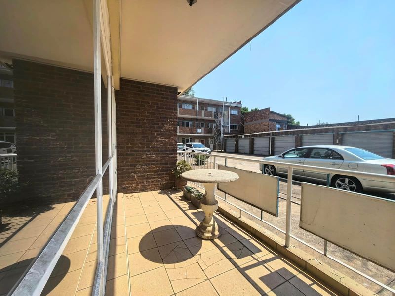 A covered balcony area featuring tiled flooring and metal railings, overlooking the apartment complex parking area.