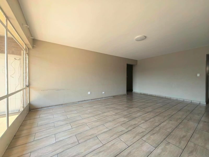 A spacious, empty living area featuring wood-look tiled flooring and a large glass sliding door providing natural light.