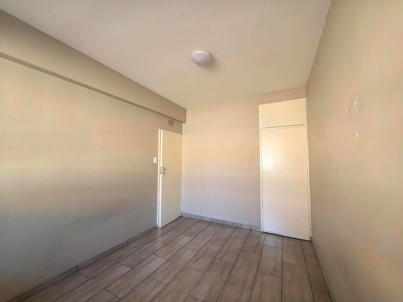 An empty bedroom featuring neutral wall tones, wood-look tiled flooring, and a built-in cupboard, providing a clean canvas for personalization.