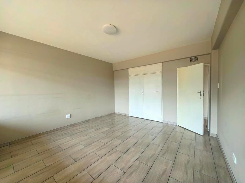 An empty bedroom featuring neutral wall tones, wood-look tiled flooring, and built-in storage cupboards.