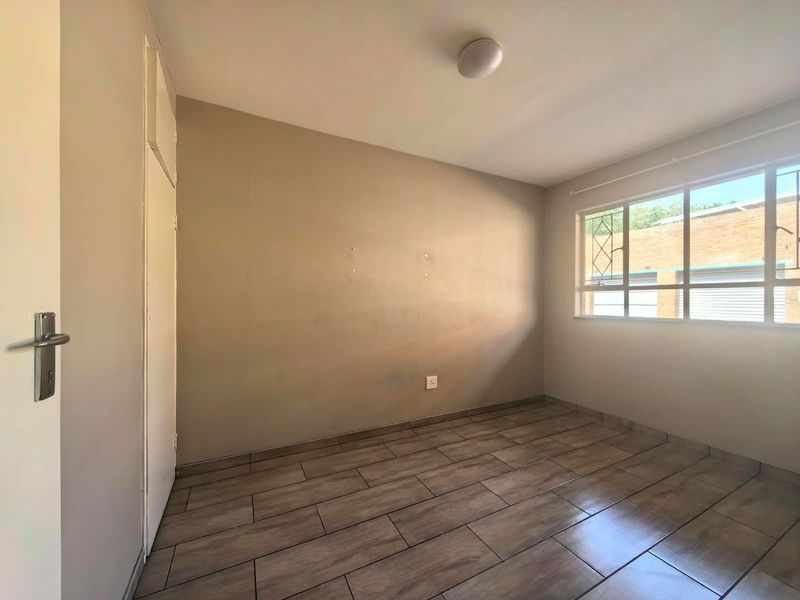 An empty bedroom featuring tiled flooring, a built-in cupboard, and a window with security bars, offering a neutral canvas for personalization.