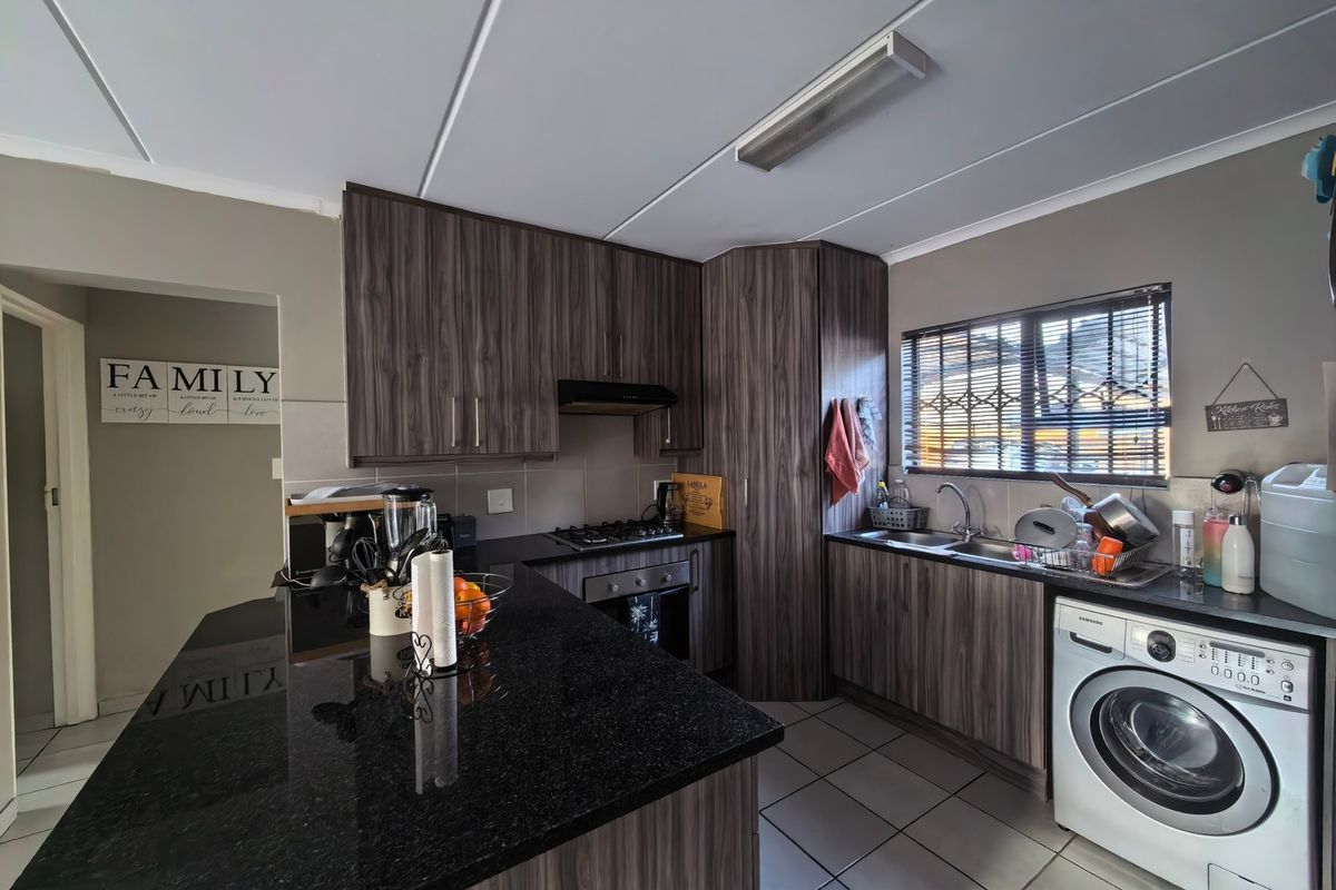 Modern kitchen featuring dark wood-look cabinetry, granite countertops, built-in oven with gas hob, and integrated laundry plumbing.