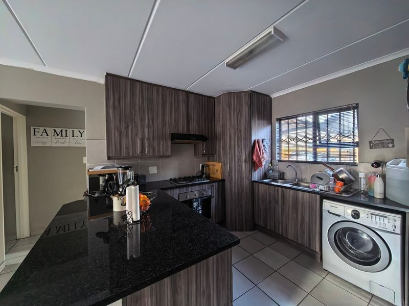 Modern kitchen featuring dark wood-look cabinetry, granite countertops, built-in oven with gas hob, and integrated laundry plumbing.