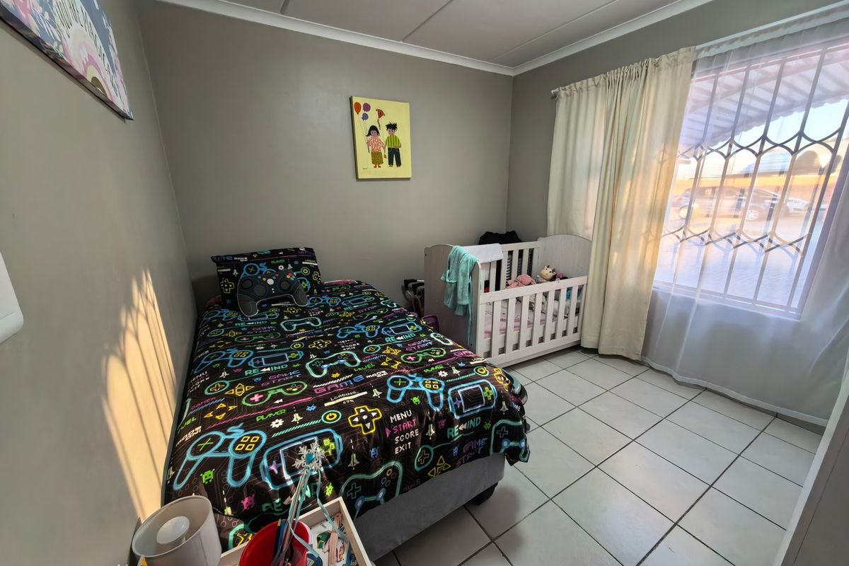 A functional bedroom featuring tiled flooring, a window with security bars, and neutral wall paint, suitable for a child's room or nursery.