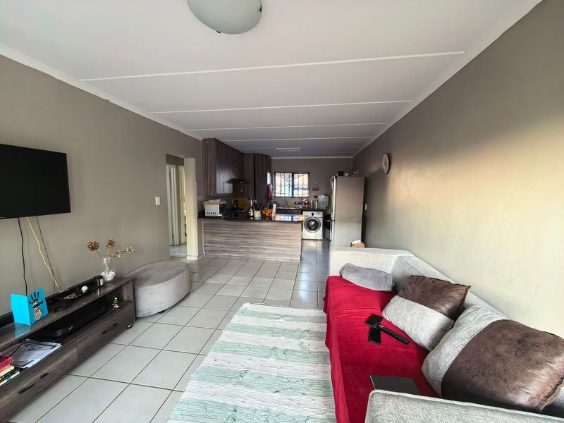 Open-plan living area featuring a kitchen with built-in cabinetry and island, seamlessly flowing into the lounge space with tiled flooring throughout.