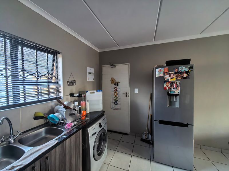 A functional kitchen area featuring a double bowl sink, laminate countertops, built-in cabinetry, and tiled flooring with a window fitted with security bars.