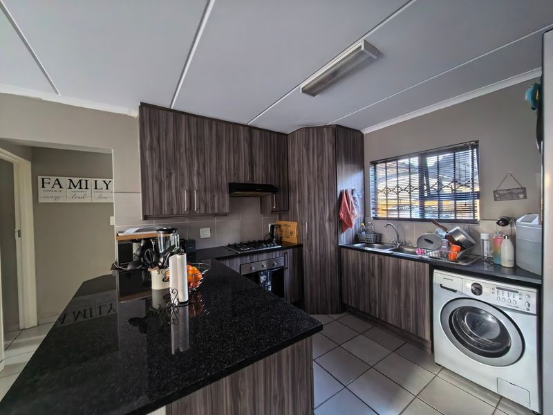 A functional kitchen featuring dark wood-grain cabinetry, granite countertops, a gas hob, and integrated laundry plumbing, complemented by tiled flooring and natural light.