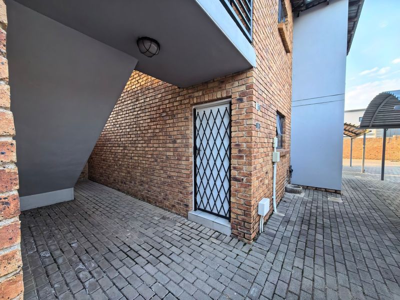 Exterior view of an apartment entrance featuring a brick facade, paved ground, and a secure metal gate.