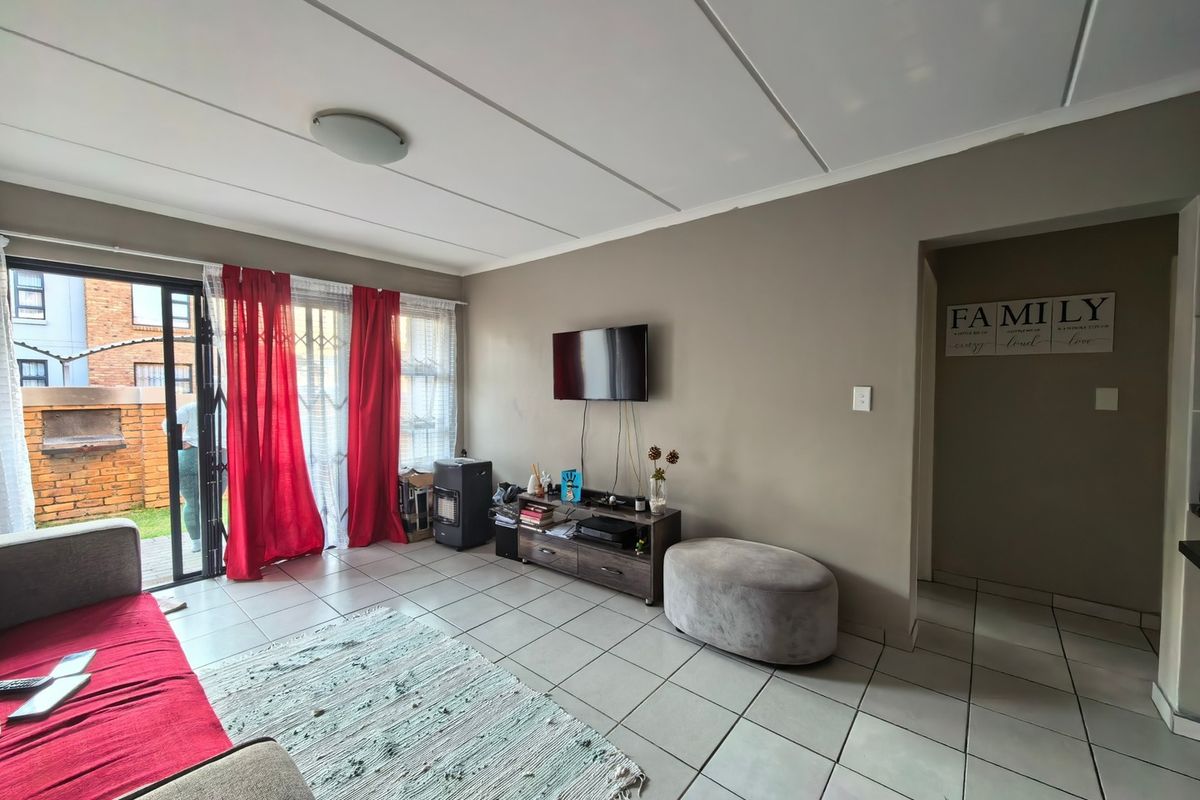 A living room featuring tiled flooring, a sliding glass door with security gate access to the exterior, and neutral wall finishes.