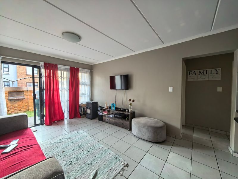 A living room featuring tiled flooring, a sliding glass door with security gate access to the exterior, and neutral wall finishes.