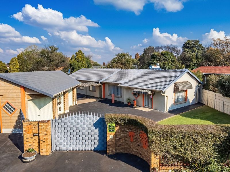 Aerial view of the property featuring a tiled roof house, double garage, paved driveway, and secure gated entrance with established garden.