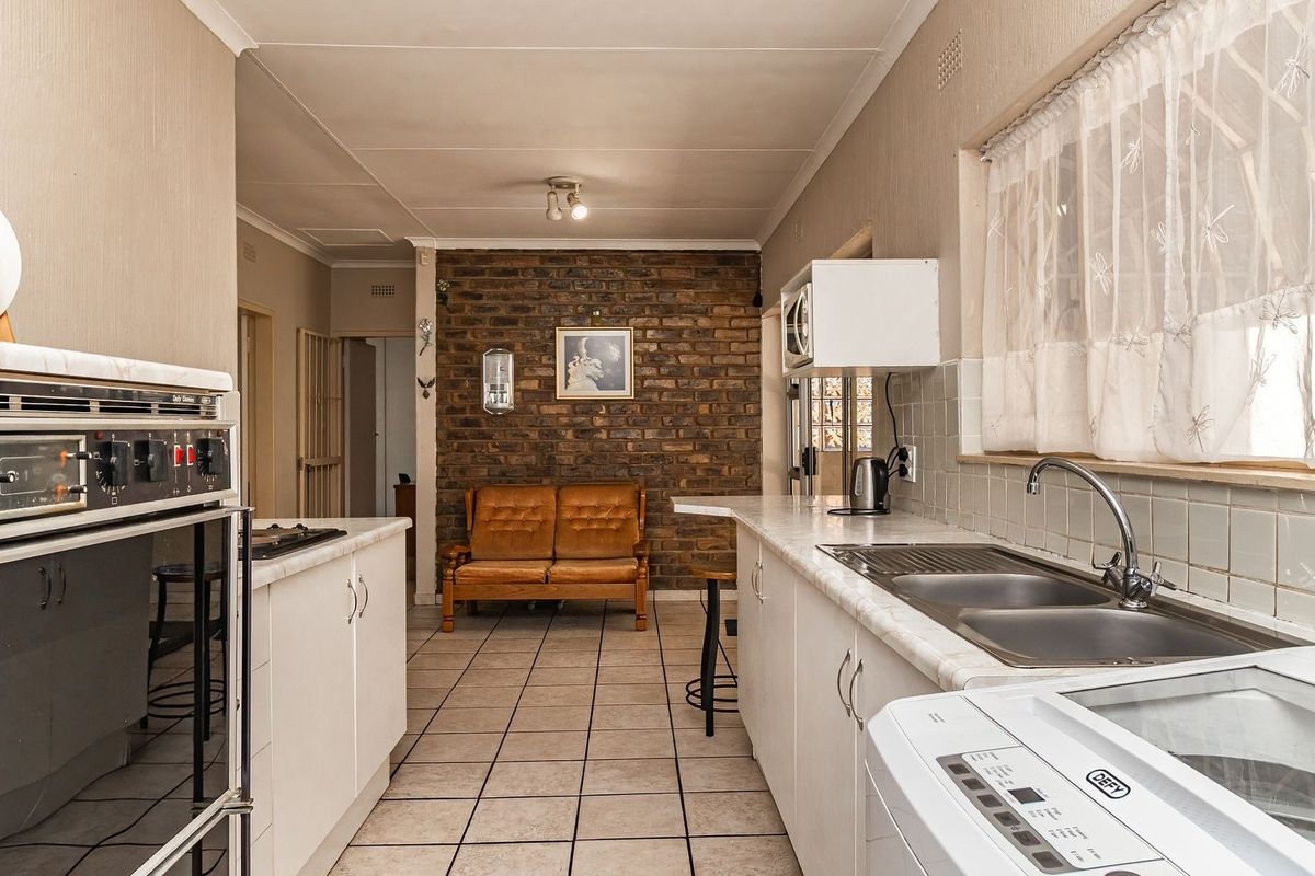 A functional kitchen featuring a built-in oven, double sink, laminate countertops, and a distinctive exposed brick feature wall with tiled flooring throughout.